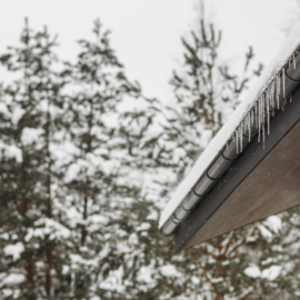 Icicles and snow on roof in Ohio with pine trees in background